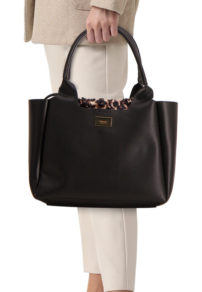 Sac à bandoulière noir par Morgan de Toi, avec doublure à motif léopard et porté à la main.
