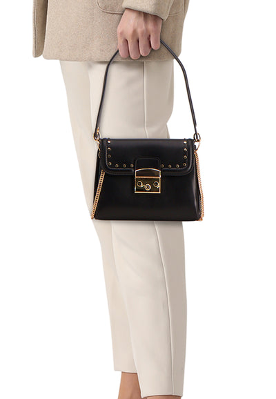 Sac à bandoulière noir de Morgan de Toi avec chaîne décorative dorée, porté avec un pantalon beige et un manteau beige.
