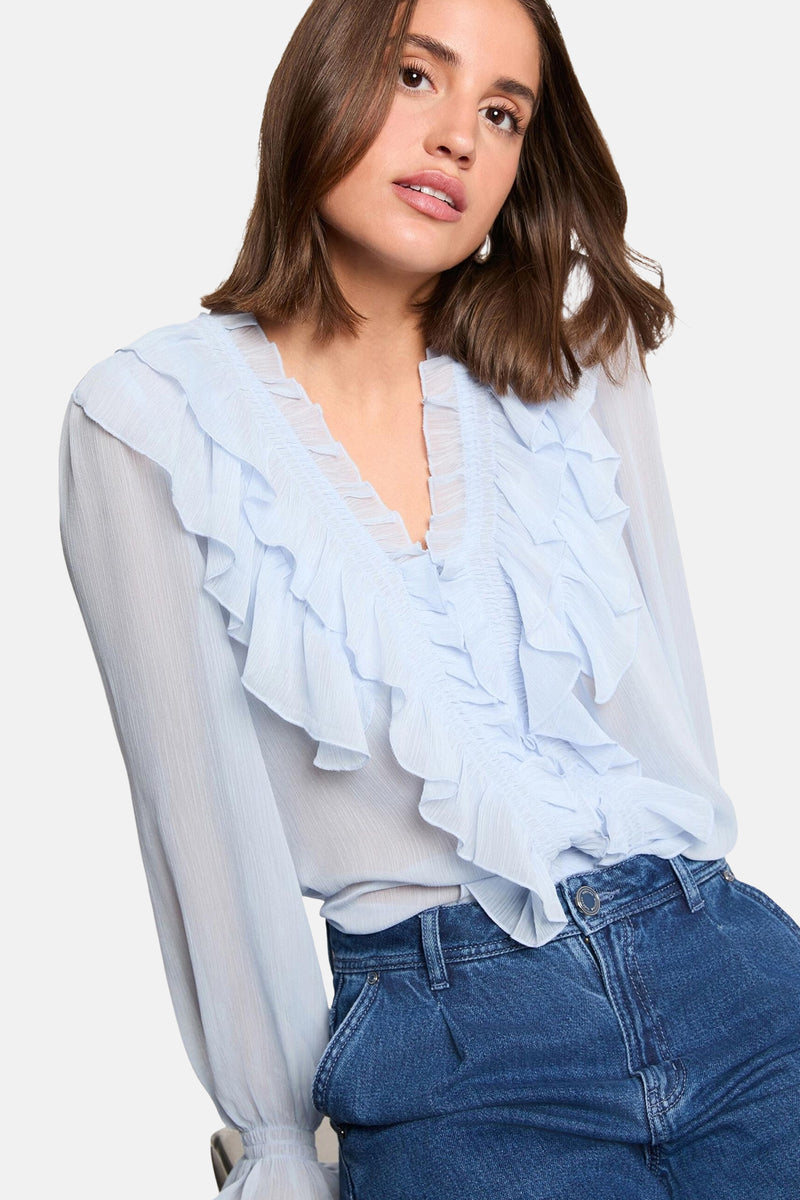 Blauwe blouse met lange mouwen van Morgan de Toi, met ruche bij de halslijn en gedragen met een high-waisted jeans.