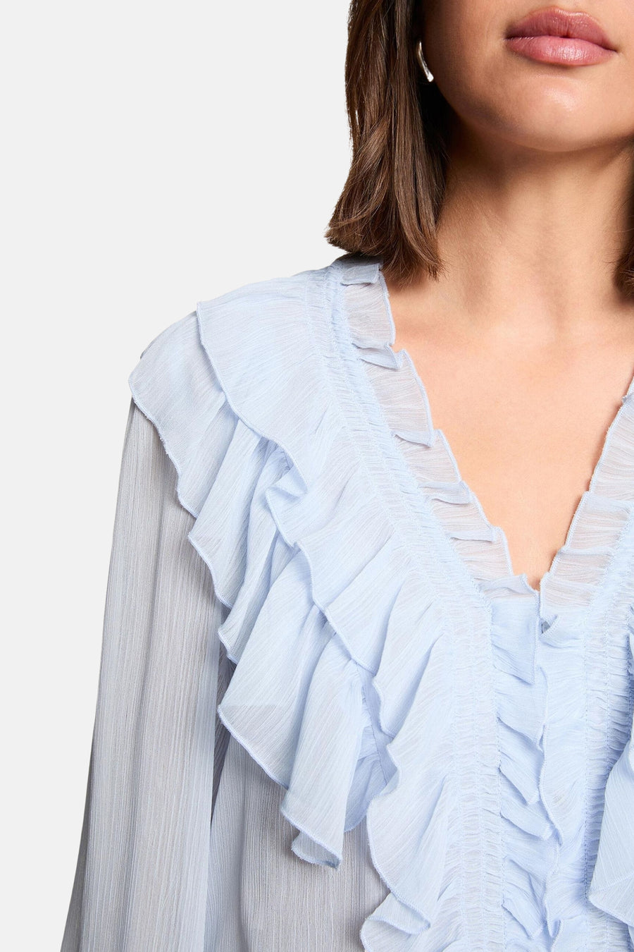 Blouse bleue à manches longues de Morgan de Toi, avec volants décoratifs sur le devant.