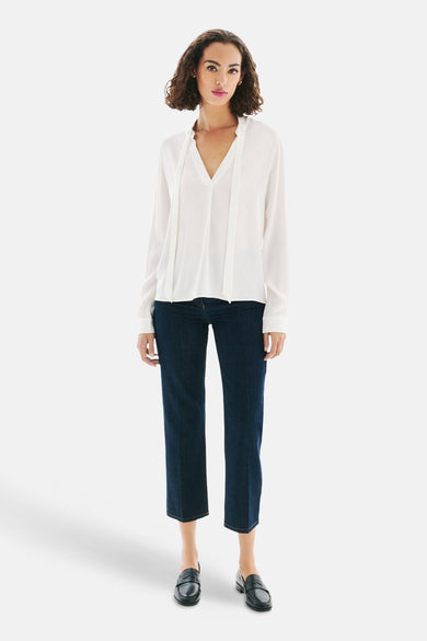 Witte blouse met lange mouwen van Caroll, gedragen met een blauwe jeans en zwarte loafers.