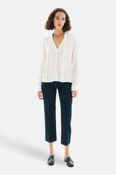 Witte blouse met lange mouwen van Caroll, gedragen met een blauwe jeans en zwarte loafers.
