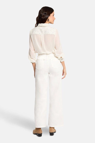 Ecru blouse met lange mouwen van Morgan de Toi, met tweed inzetstuk en gedragen met een witte jeans en bruine enkellaarsjes.