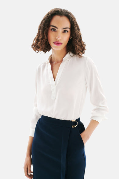 Chemisier blanc à manches longues de CAROLL, avec col classique et patte de boutonnage, porté avec une jupe bleu marine.

