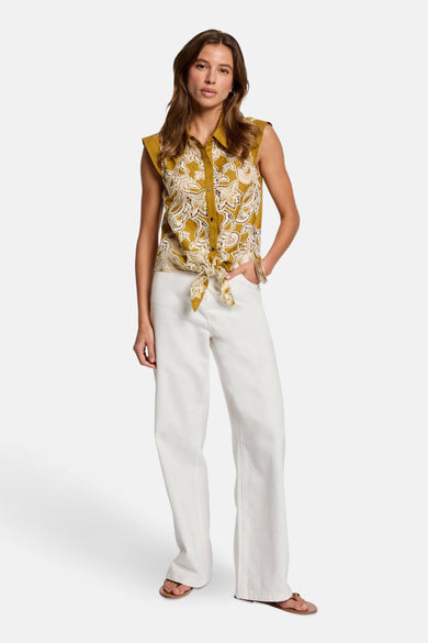 Chemisier jaune sans manches de Morgan de Toi avec imprimé floral et noué à la taille, porté avec un pantalon blanc.
