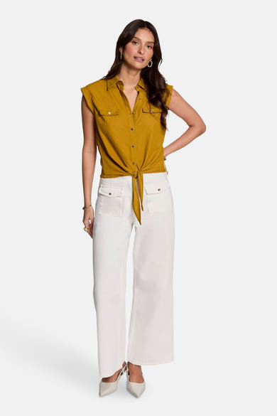 Chemisier sans manches jaune de Morgan de Toi, noué à la taille, porté avec un pantalon blanc et des escarpins clairs.
