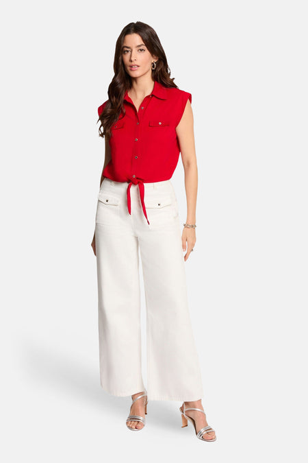 Chemisier rouge sans manches de Morgan de Toi avec col, poches poitrine et nœud à la taille, porté avec un pantalon blanc.
