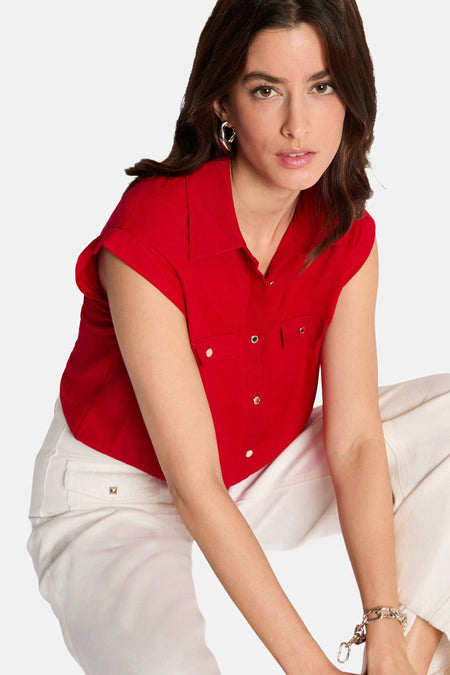 Chemisier rouge sans manches de Morgan de Toi avec col et poches poitrine à boutons argentés, porté avec un pantalon blanc.