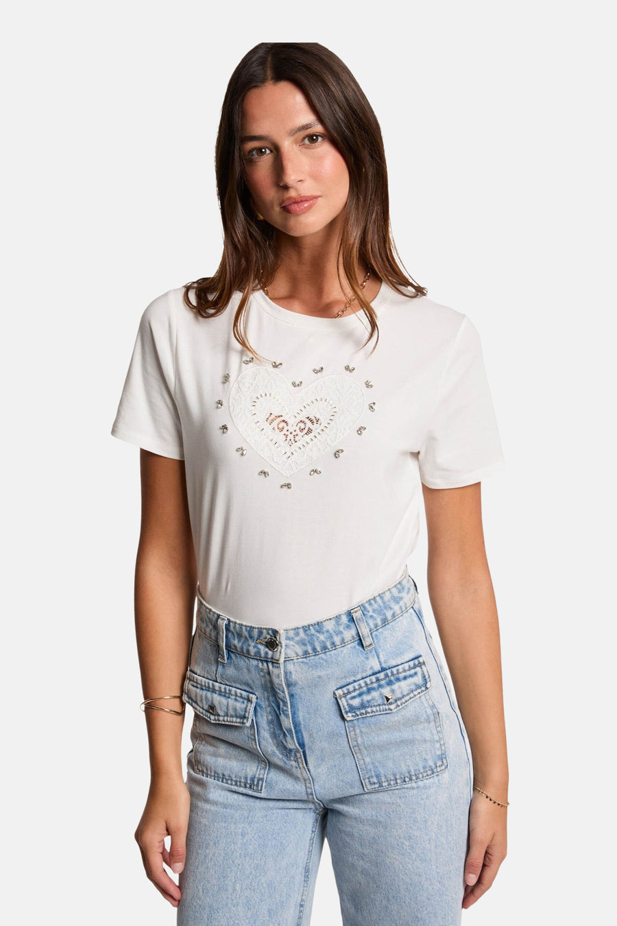 T-shirt blanc à manches courtes de Morgan de Toi orné d'un cœur en dentelle et de studs, porté avec un jean bleu.
