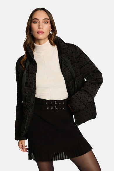 Veste courte noire de Morgan de Toi, avec motif monogramme discret, portée avec un pull blanc et une jupe noire plissée.
