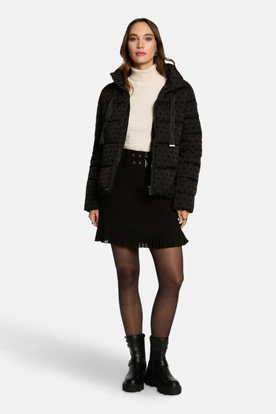 Veste courte noire de Morgan de Toi, avec motif matelassé, portée avec un col roulé et une jupe noire.
