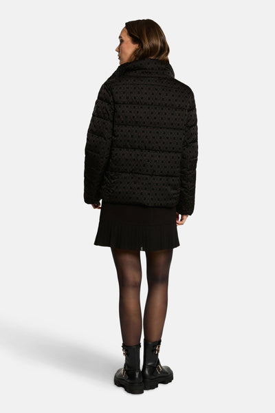 Veste courte noire de Morgan de Toi avec motif répété, portée avec une jupe noire plissée et des bottines noires.
