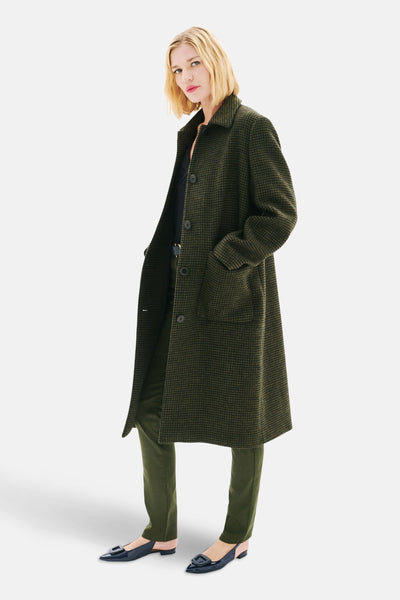 Veste longue verte à carreaux de Caroll, portée avec un pantalon et des chaussures noirs, modèle sur fond blanc.
