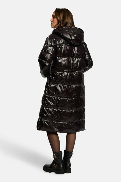 Veste longue noire de Morgan de Toi, avec capuche et motif matelassé brillant, portée avec des collants et des bottes noires.
