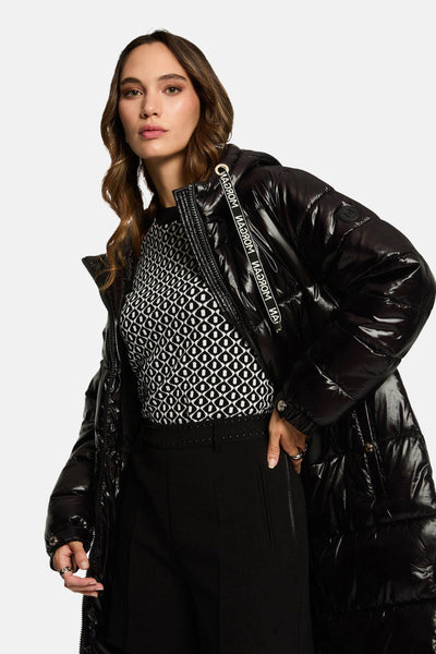 Veste longue noire de Morgan de Toi, style matelassé et brillante, portée sur un pull à motifs géométriques.