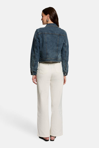 Veste en jean bleu moyen de Morgan de Toi, vue de dos, portée avec un pantalon blanc et des sandales noires.