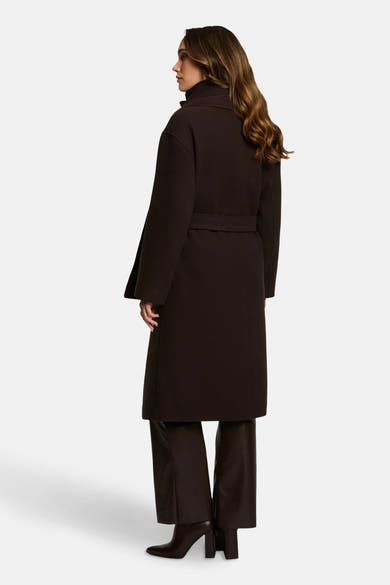 Lange bruine jas van Morgan de Toi, met riem, gecombineerd met een bruine broek en enkellaarsjes.