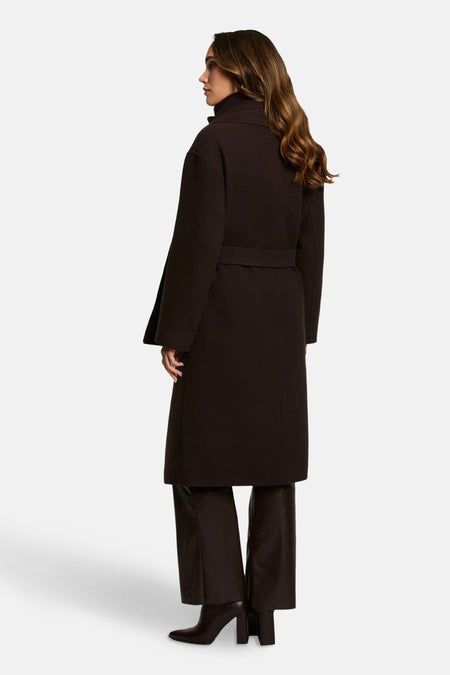 Lange bruine jas van Morgan de Toi, met riem, gecombineerd met een bruine broek en enkellaarsjes.