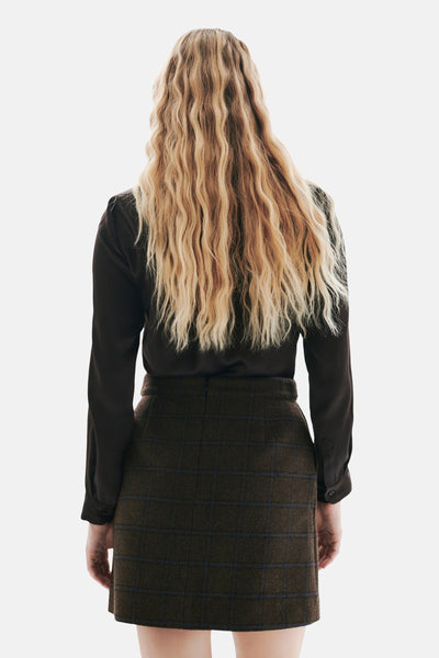 Jupe courte brune à carreaux par CAROLL, avec une chemise marron à manches longues et des cheveux blonds ondulés.
