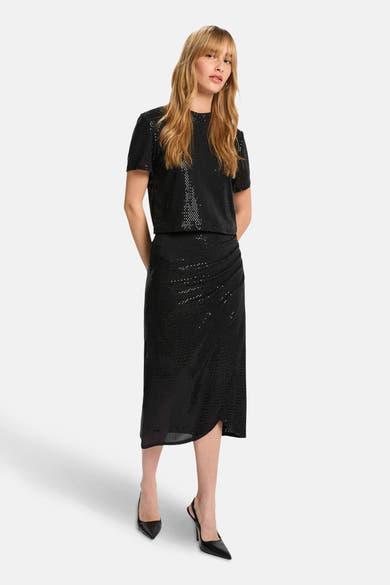 Jupe 3/4 noire de Morgan de Toi avec effet drapé et fente, portée avec un haut scintillant et des escarpins noirs.