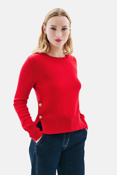 Rode ronde hals trui van CAROLL, met decoratieve knoopsluiting aan de taille, gedragen met een blauwe jeans.