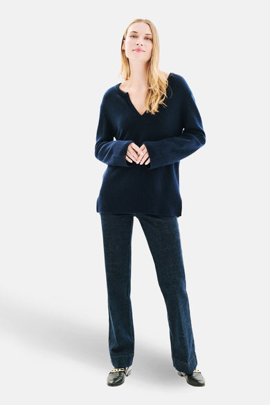 Blauwe V-hals trui van Caroll, gedragen met een donkerblauwe spijkerbroek en zwarte loafers met gouden ketting.