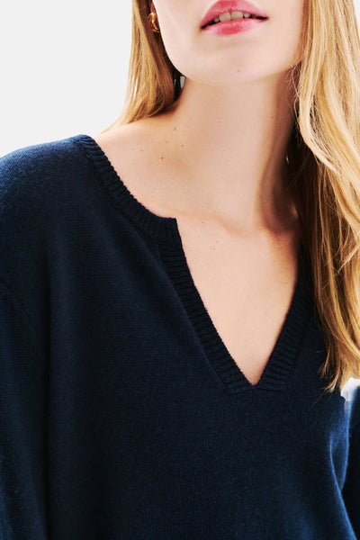 Pull à col en V bleu de CAROLL avec un col dégagé, porté avec des boucles d'oreilles dorées.