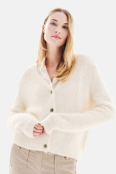 Witte, pluizige gebreide cardigan van CAROLL, met een beige broek en zwarte hakken.