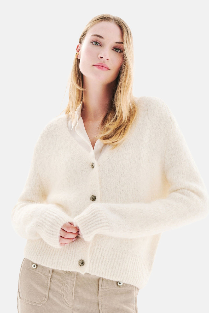 Witte, pluizige gebreide cardigan van CAROLL, met een beige broek en zwarte hakken.