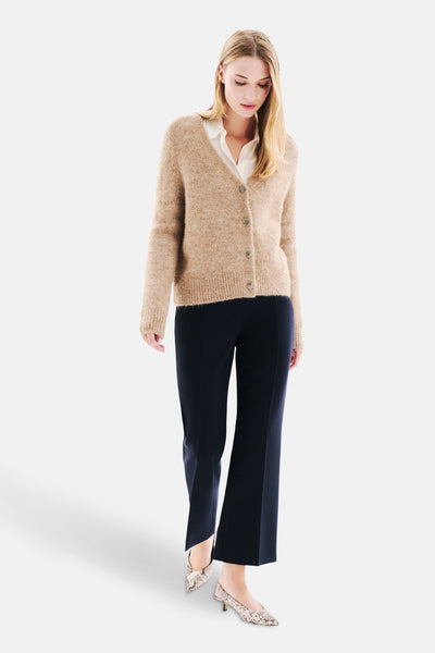 Beige gebreid vest van CAROLL, gedragen over een wit overhemd met een marineblauwe broek en slangenprint pumps.