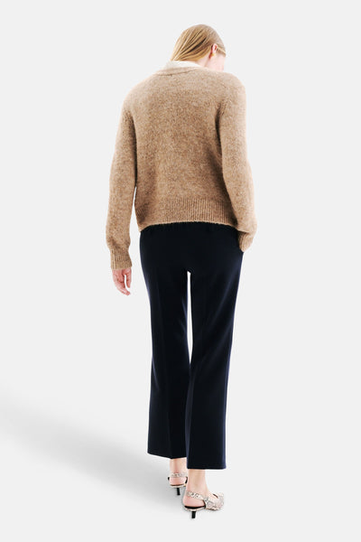 Cardigan beige de CAROLL, à manches longues, porté avec un pantalon bleu marine et des chaussures à imprimé serpent.