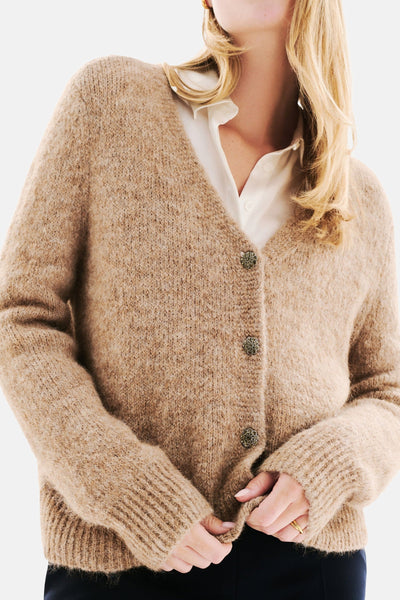 Beige gebreid vest van CAROLL, met decoratieve knopen en gedragen over een wit overhemd.