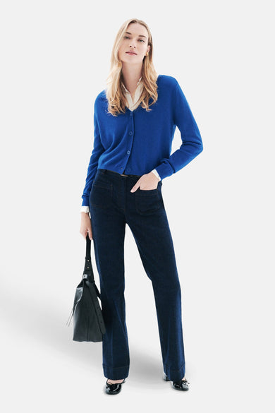 Blauwe cardigan van CAROLL, gedragen over een wit overhemd, met een spijkerbroek en een zwarte tas.