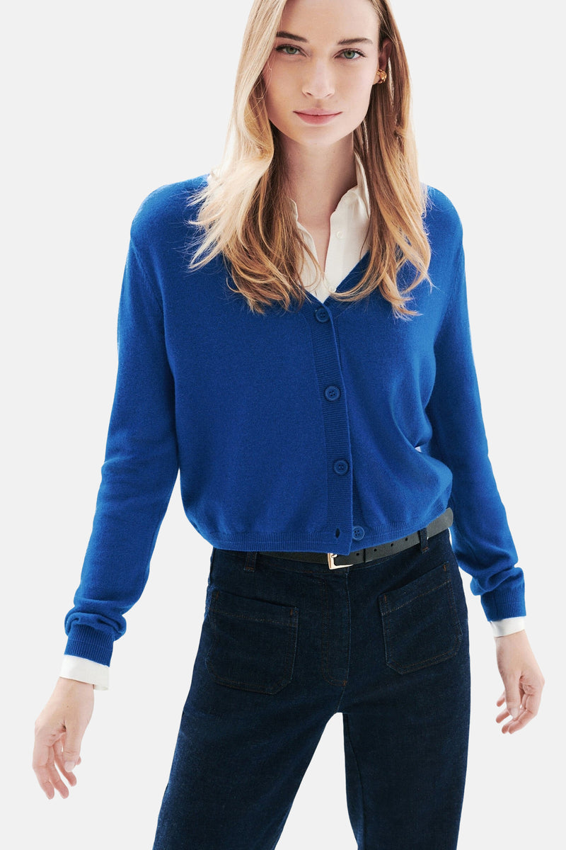 Blauwe cardigan van CAROLL, gedragen over een wit overhemd en een donkere spijkerbroek met een zwarte riem.