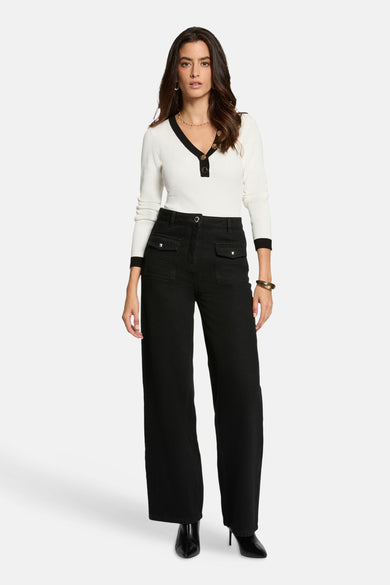 Witte V-hals trui van Morgan de Toi, met decoratieve knopen, gedragen met een zwarte pantalon met hoge taille.