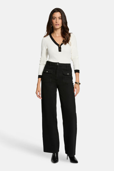 Witte V-hals trui van Morgan de Toi, met decoratieve knopen, gedragen met een zwarte pantalon met hoge taille.
