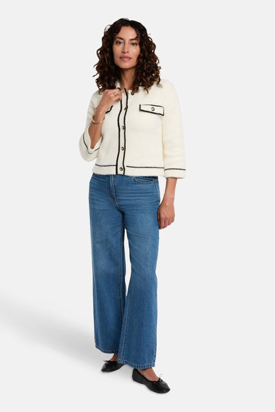 Witte gebreide gilet van Morgan de Toi, met zwarte bies en gouden knopen, gedragen met een uitlopende jeans.