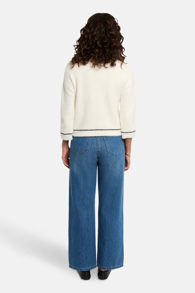 Witte, pluizige gebreide gilet van Morgan de Toi, met zwarte bies en gedragen over een wijde blauwe broek.