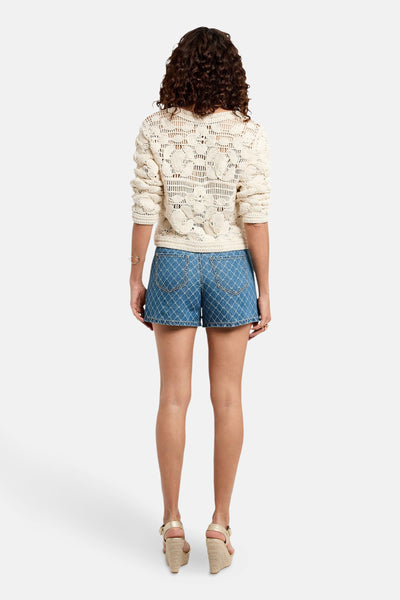 Gilet écru de Morgan de Toi avec motif ajouré, porté avec un short en jean et des chaussures compensées dorées.
