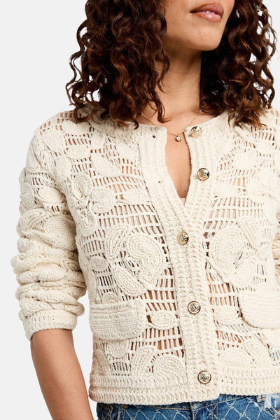Gilet écru de Morgan de Toi, avec motifs crochetés et boutons dorés, porté sur un débardeur.