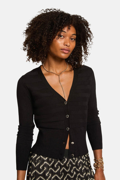 Zwarte cardigan met knopen van Morgan de Toi, gedragen met een gouden ketting en een rok met abstract patroon.