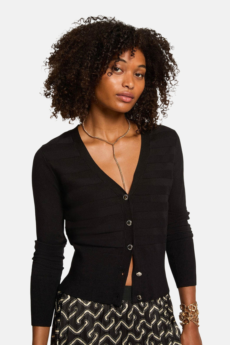 Zwarte cardigan met knopen van Morgan de Toi, gedragen met een gouden ketting en een rok met abstract patroon.