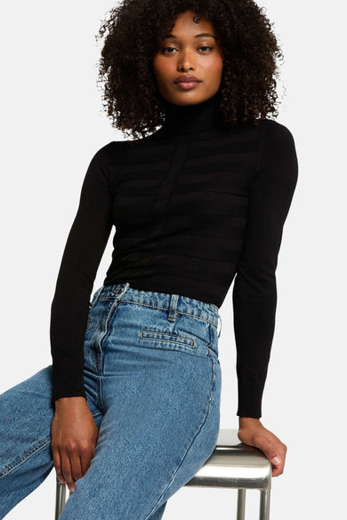 Zwarte coltrui van Morgan de Toi, met horizontale patronen en gedragen met een blauwe jeans.