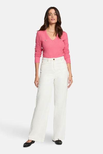 Roze trui met V-hals van Morgan de Toi, met decoratieve knopen en gedragen met een witte broek.