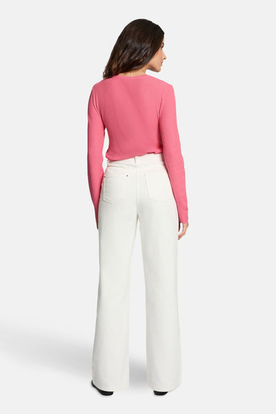 Roze rondehals trui van Morgan de Toi, met lange mouwen, gedragen met een witte broek met hoge taille.