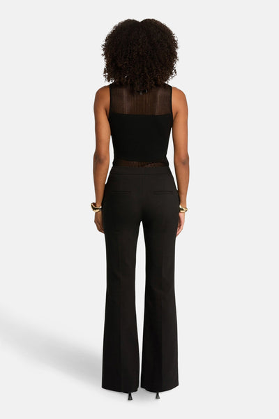 Débardeur noir Morgan de Toi, à empiècement transparent au niveau du cou et de la taille, porté avec un pantalon noir et des bracelets dorés.