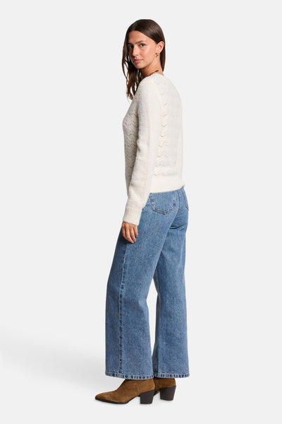 Witte V-hals trui van Morgan de Toi, met ajourpatronen, gedragen met een wijde blauwe jeans en bruine enkellaarsjes.