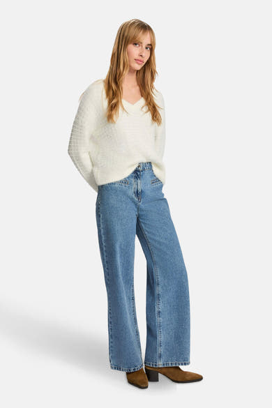 Witte V-hals trui van Morgan de Toi, in een getextureerde breisel, gedragen met een high-waisted jeans en bruine enkellaarsjes.