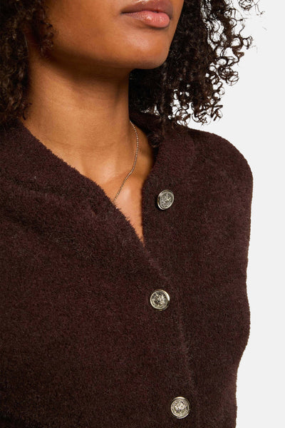 Cardigan marron en maille bouclée de Morgan de Toi avec boutons décoratifs dorés et chaîne dorée au cou.
