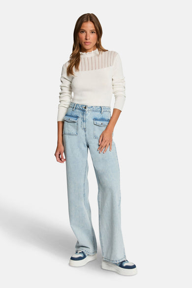 Witte rondehals trui van Morgan de Toi, met ajour detail, gedragen met een lichtblauwe high-waist jeans en sleehak sneakers.